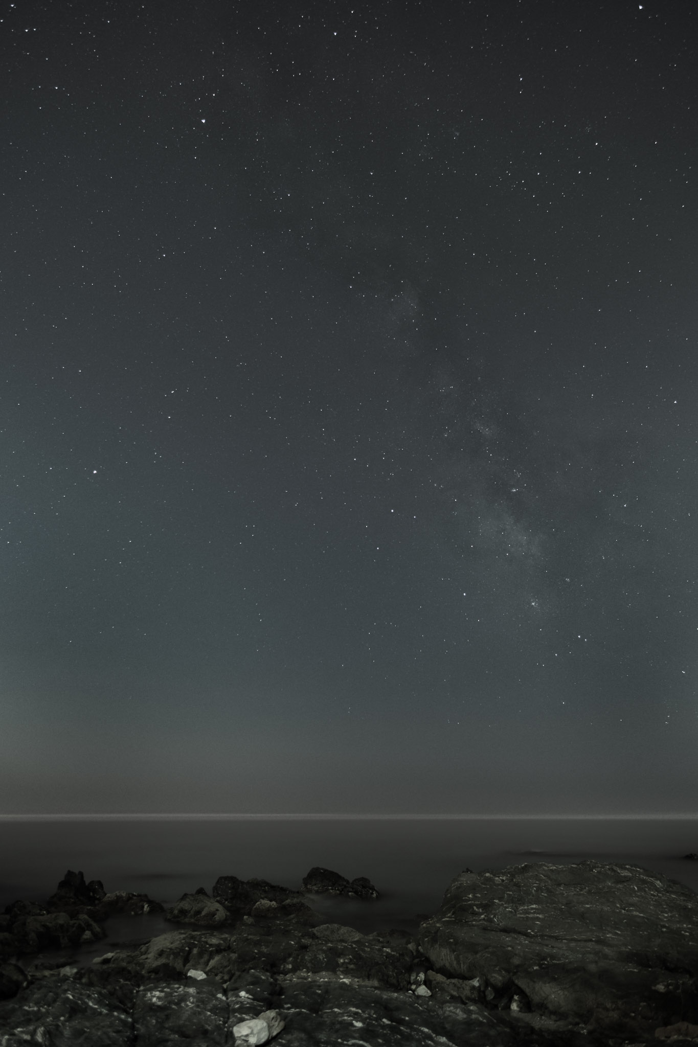 The Milky Way is just barely visible over the sea and rocky shore